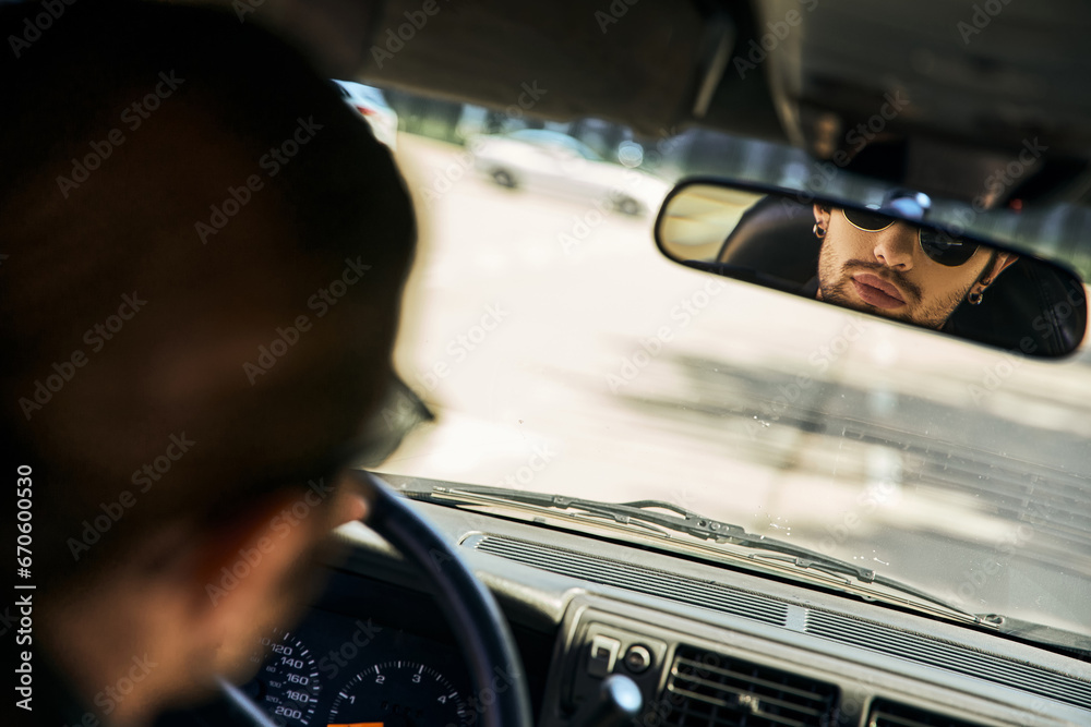 handsome sexy male model with sunglasses behind steering wheel and looking in rearview mirror - obrazy, fototapety, plakaty 