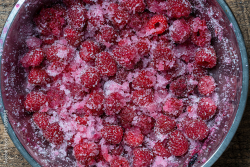 Fresh red raspberry berry, covered with granulated sugar for jam preparation in bowl, top view, closeup. Background and texture of raspberries with sugar