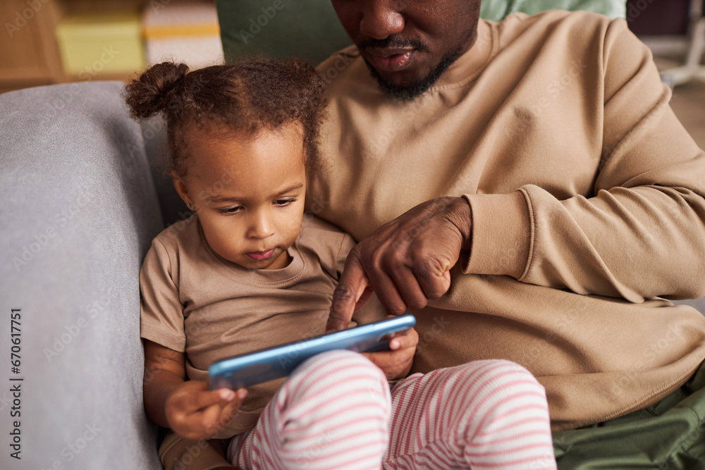 Close up of father teaching Black little girl using smartphone while sitting together on sofa at home, copy space Close up of father teaching Black little girl using smartphone while sitting together on sofa at home, copy space