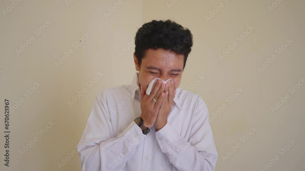 Young Indonesian curly man wear white clothes with influenza symptom and sneeze with tissue. The footage is suitable to use for health care content media and man expression advertising. Young Indonesian curly man wear white clothes with influenza symptom and sneeze with tissue. The footage is suitable to use for health care content media and man expression advertising.