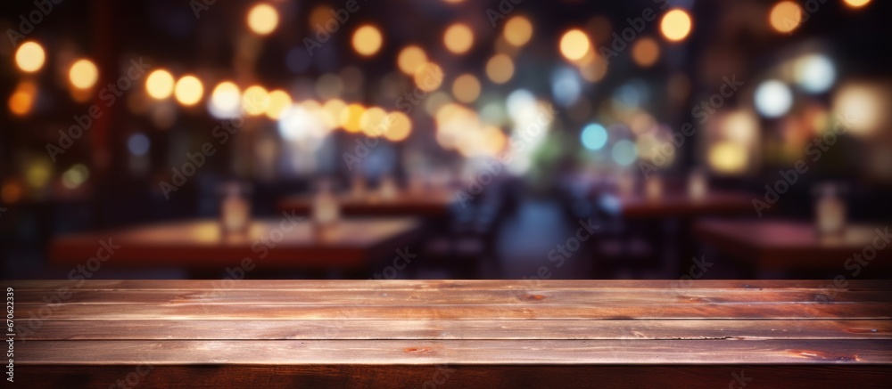 Empty wooden table with a blurred nighttime restaurant backdrop.
