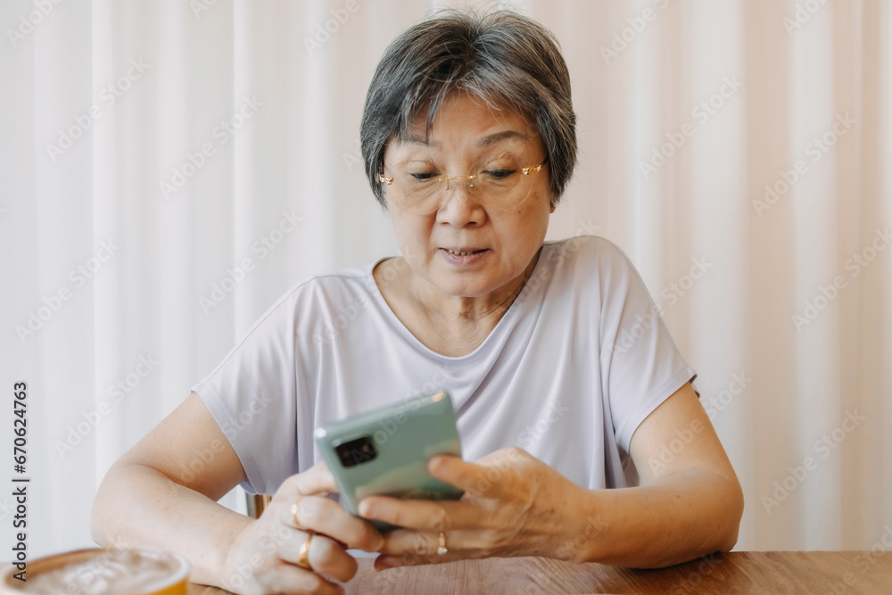Happy asian old woman smiling and using phone for chatting, reading news and looking at tablet mobile, sitting on chair alone over white curtain. Happy asian old woman smiling and using phone for chatting, reading news and looking at tablet mobile, sitting on chair alone over white curtain.