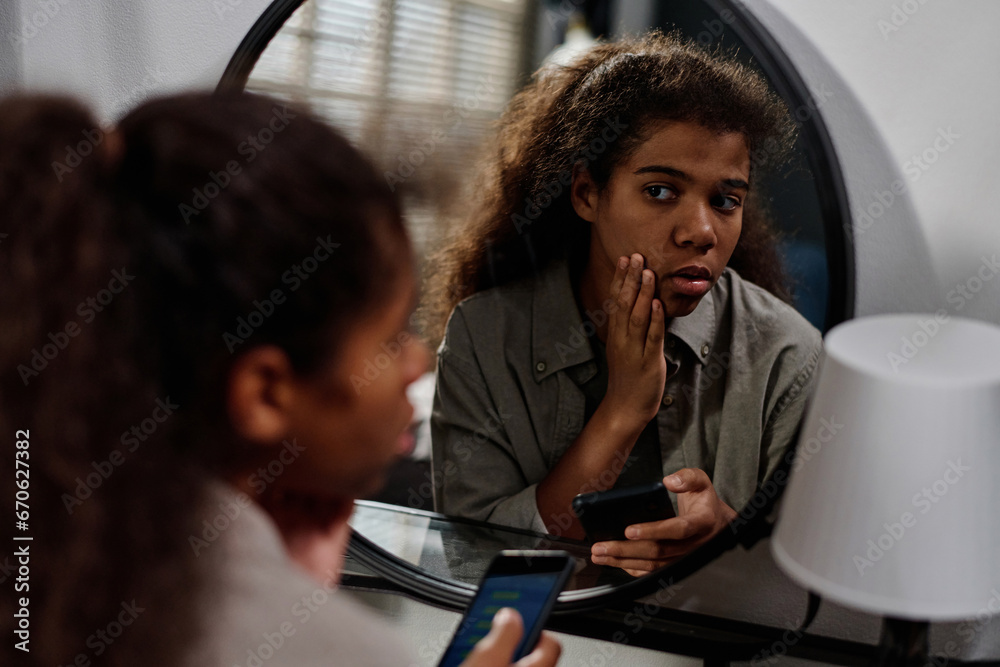 Stressed African American teenage girl touching her face and looking in ...