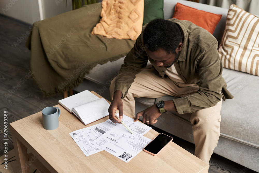 High angle portrait of Black adult man doing taxes at home and filling out documents, copy space - obrazy, fototapety, plakaty 