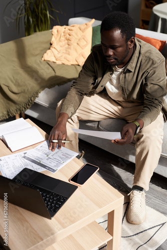 High angle portrait of adult Black man using laptop while doing taxes and home and calculating budget