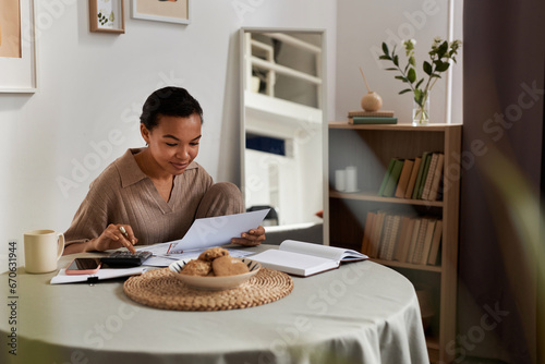 Minimal portrait of smiling young Black woman doing taxes at home and managing household, copy space