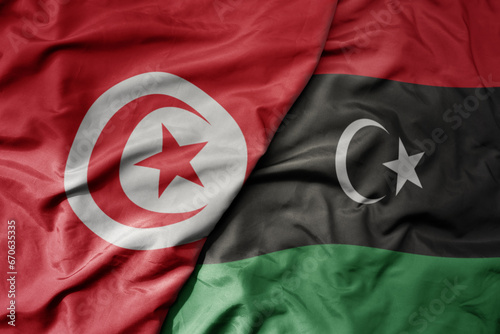 big waving national colorful flag of tunisia and national flag of libya .