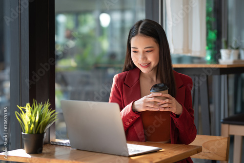 Asian business woman drinking a coffee working on laptop at cafe.