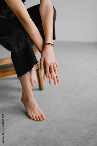 Partial view of barefoot woman in dark jeans touching hands near step stool on grey