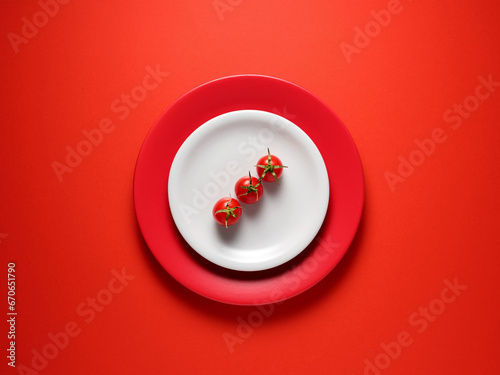 Fresh cherry tomatoes on a plate with red background. Top view, copy space. Creative food concept. © Cagkan
