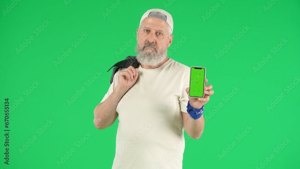 Portrait of senior man hipster on Chroma key green screen background, man in white t-shirt holding smartphone looks cool at camera. Advertising area, workspace mockup. Portrait of senior man hipster on Chroma key green screen background, man in white t-shirt holding smartphone looks cool at camera. Advertising area, workspace mockup.