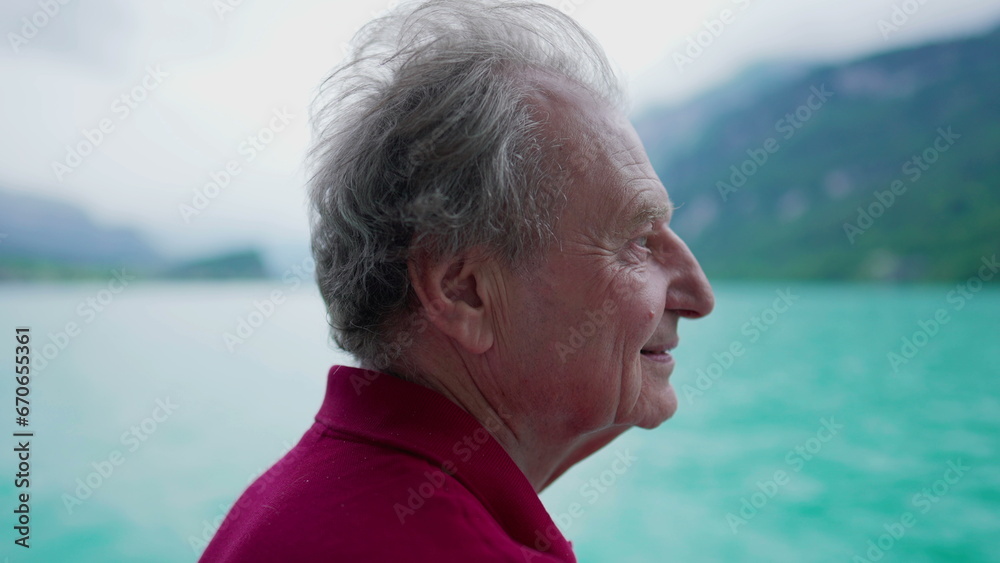 Carefree senior man enjoying serene nature's view of lake and mountains while traveling by boat, profile close-up face of senior person in 70s contemplating and exploring new horizons
