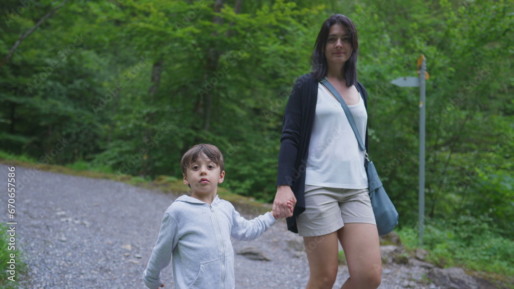 Mother and child holding hands walking in trail path in forest. Mom and son hiking in outdoors, weekend family activity, adventurous journey concept