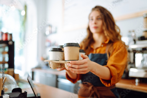 Young female barista holding disposable glasses with hot drink to go. Takeaway delivery concept. Takeaway food concept, business.