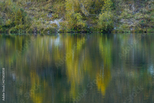 Picturesque water surface of a mountain lake with a beautiful mirror reflection of trees in the water