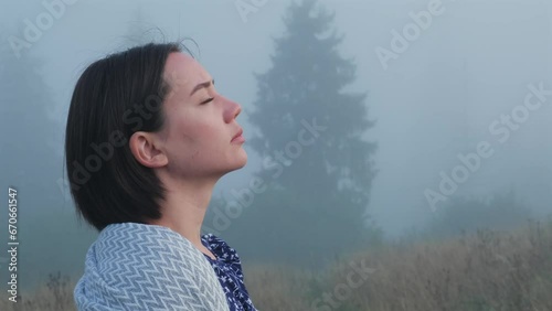 Young woman makes deep breath outdoors. Beautiful relaxed girl portrait on misty morning in field in mountains. Cinematic shot