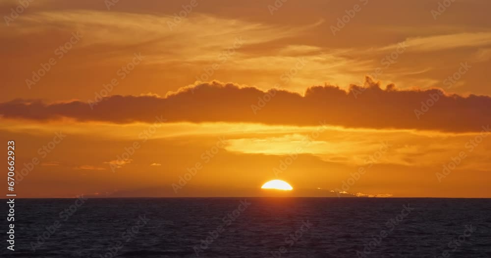 Sunset over sea horizon behind island timelaps, close up big sun setting ocean water laps backgroung