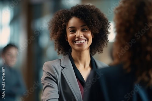 African American businesswoman with kinky hair smiles greeting colleagues. Joyful young woman in formal wear shakes hand of co-worker.
