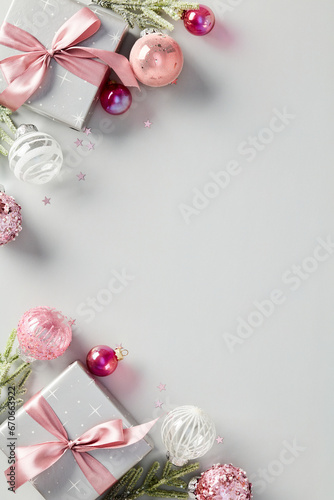 Christmas poster template. Flat lay composition with stylish gift boxes decorated pink ribbon bow, baubles, confetti, fir branches on gray background.