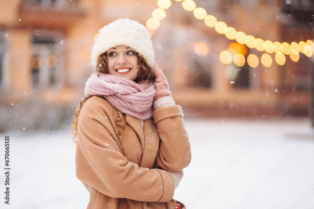 Happy woman in winter clothes walks at the Christmas market. Curly-haired woman enjoying winter holidays on a snowy city street. Light all around. Happy woman in winter clothes walks at the Christmas market. Curly-haired woman enjoying winter holidays on a snowy city street. Light all around.