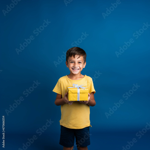 Boy in yellow t-shirt smiling with a gift in his hands on a blue background