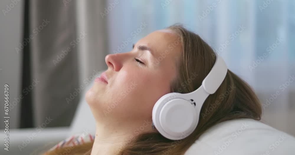 Young woman relaxing on comfortable sofa with closed eyes wearing headphones Young woman relaxing on comfortable sofa with closed eyes wearing headphones