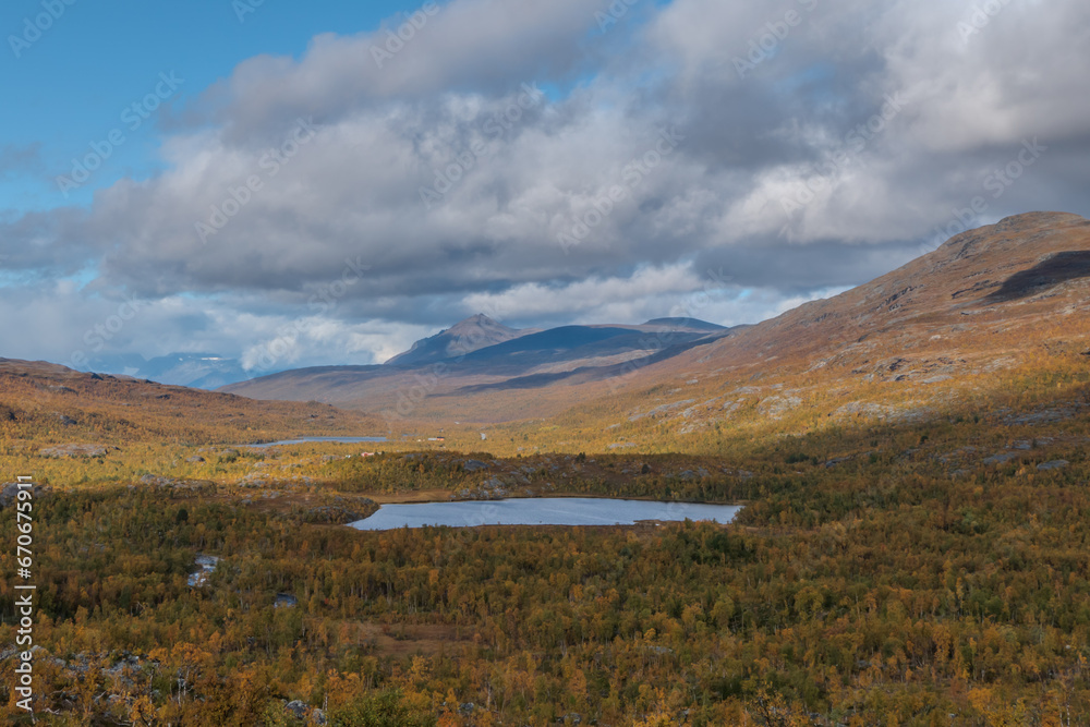 A small lake in the middle of autumn colored wilderness. Mountains on the background. Blue sky and white clouds