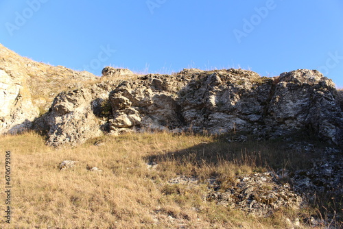 A rocky hill with grass and a blue sky