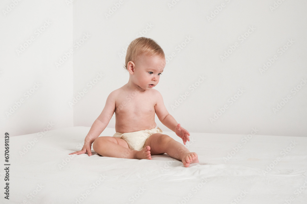 Happy baby in panties is playing on white bed in white room