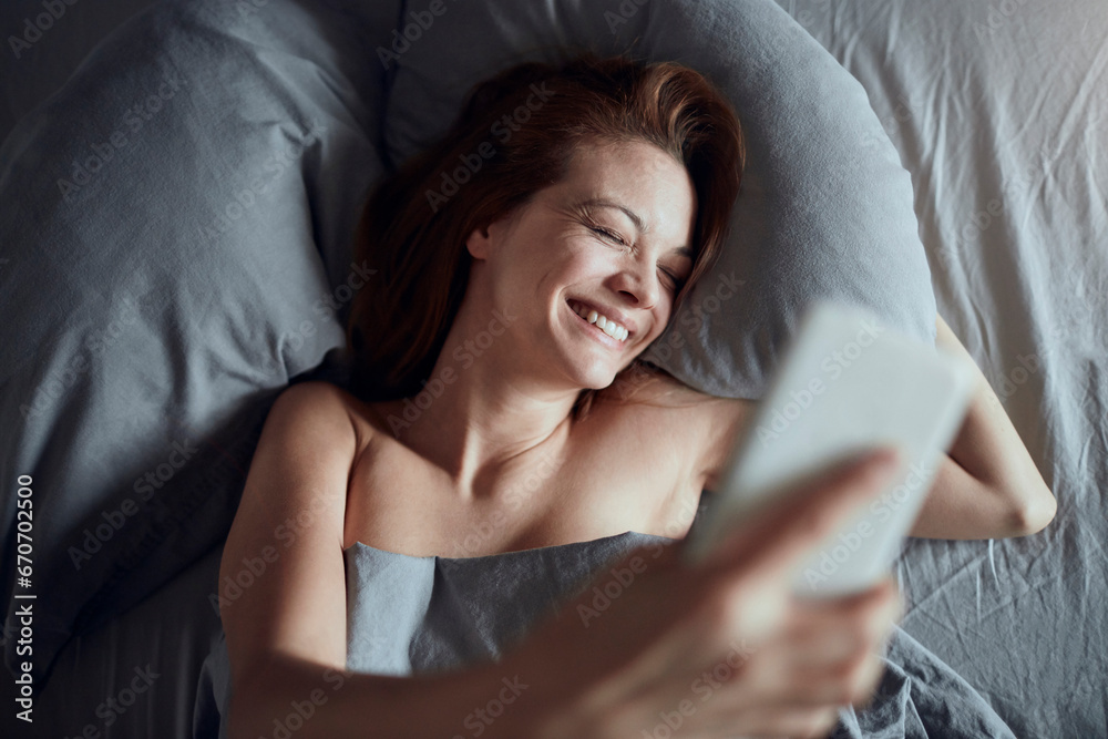Happy young woman using the smartphone in the morning after waking up in her bed Happy young woman using the smartphone in the morning after waking up in her bed