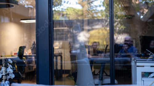 Blurred view through a glass window showing an office interior with people working inside. This image captures the modern workplace environment and teamwork.
