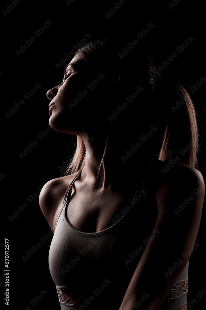 Naklejka premium Beautiful caucasian girl posing yoga in shadow. side lit photo on black background.