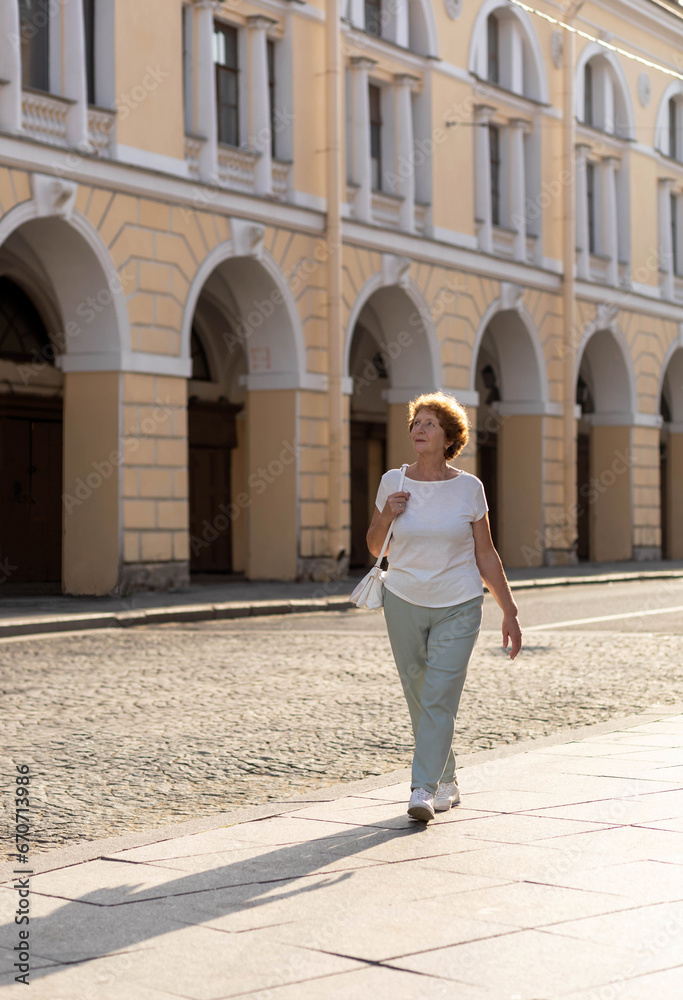 An older woman walks down the street on a sunny summer day.