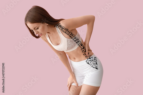 Young woman suffering from back pain on pink background photo