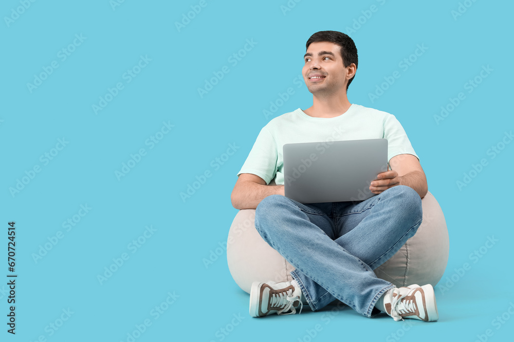 Male programmer with laptop sitting on blue background