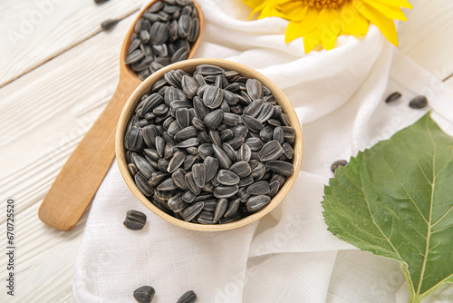 Bowl and spoon with sunflower seeds on white wooden background