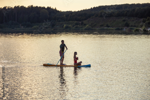 Woman meditating on supboard early morning with man paddling.