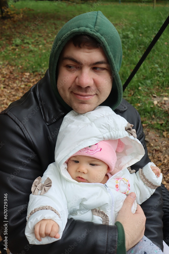 dad holds a little girl in his arms and rides on a swing in the park in autumn dad holds a little girl in his arms and rides on a swing in the park in autumn