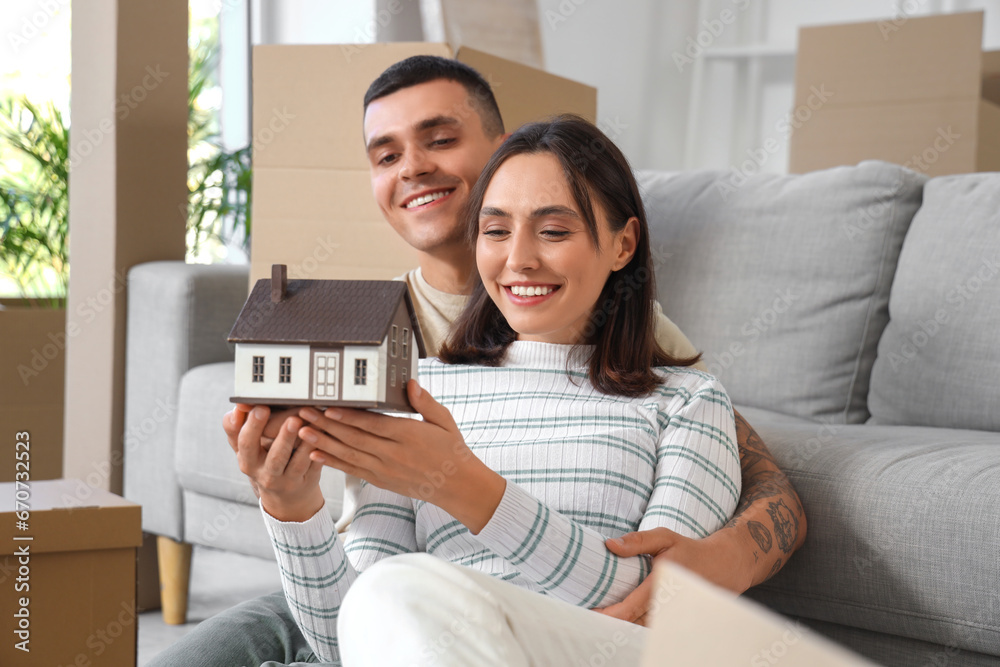 Happy young couple with house model in room on moving day Happy young couple with house model in room on moving day