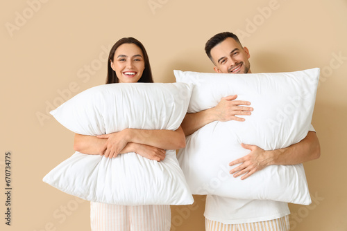 Young couple with soft pillows on beige background