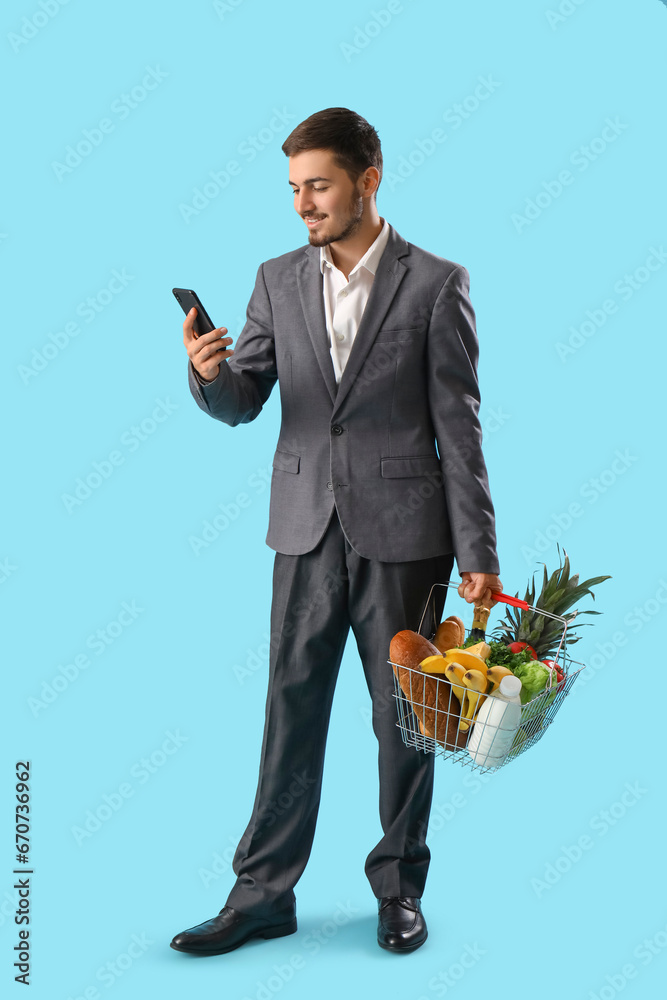 Young man with shopping basket and mobile phone on blue background Young man with shopping basket and mobile phone on blue background