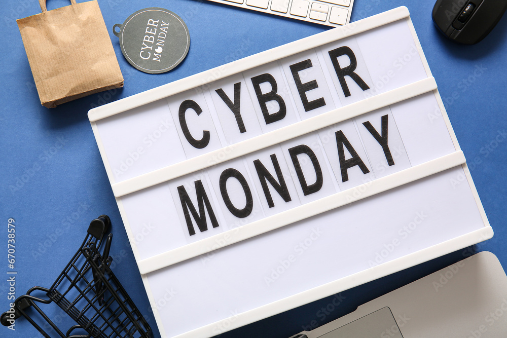 Board with text CYBER MONDAY, small shopping cart and bag on blue background, closeup Board with text CYBER MONDAY, small shopping cart and bag on blue background, closeup