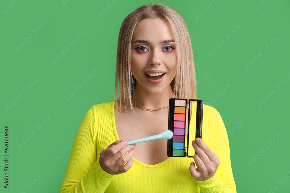 Beautiful young woman with brush and palette of colorful eyeshadows on green background Beautiful young woman with brush and palette of colorful eyeshadows on green background