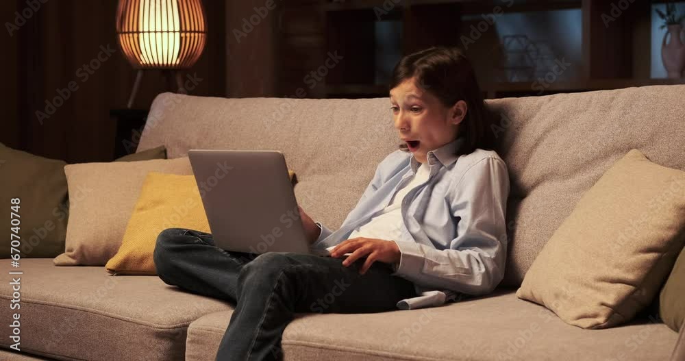 Young boy sits on the sofa, completely engrossed in the news displayed on laptop. His eyes are fixed on the screen, absorbing the latest updates and information with keen interest. Young boy sits on the sofa, completely engrossed in the news displayed on laptop. His eyes are fixed on the screen, absorbing the latest updates and information with keen interest.