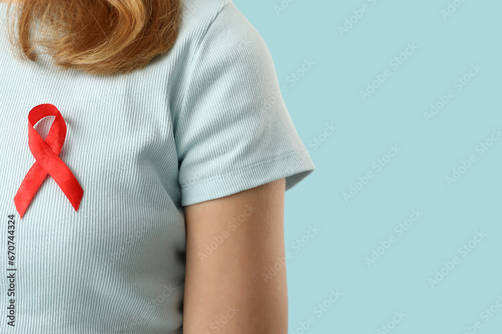 Young woman with red ribbon on blue background, closeup. AIDS concept Young woman with red ribbon on blue background, closeup. AIDS concept