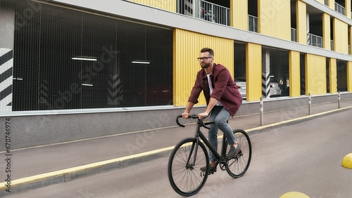 Bike Everywhere. Side view of handsome man with stubble in casual clothes riding on his bicycle along a road against yellow building
