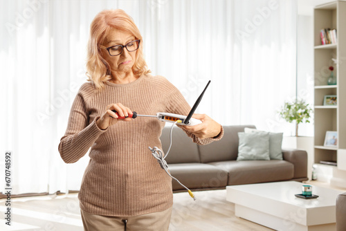 Confused mature woman trying to fix a router with a screwdriver