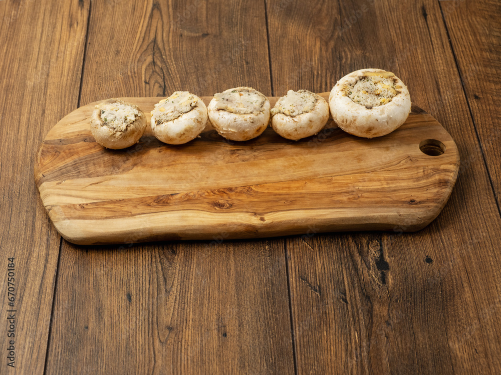 Stuffed mushrooms cups on a wooden board and table. High quality product with breadcrumbs, cheese and herbs ready for oven cooking. Stuffed mushrooms cups on a wooden board and table. High quality product with breadcrumbs, cheese and herbs ready for oven cooking.