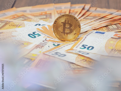 Golden bitcoin standing on euro bank notes foreground out of focus. Time to invest into crypto currency concept. Economy and financial background. Get rich theme.