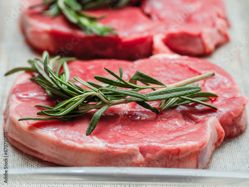 Juicy uncooked lamb leg steak with green fresh rosemary on plastic tray. Uncooked high quality meat product with rich taste and vivid color.